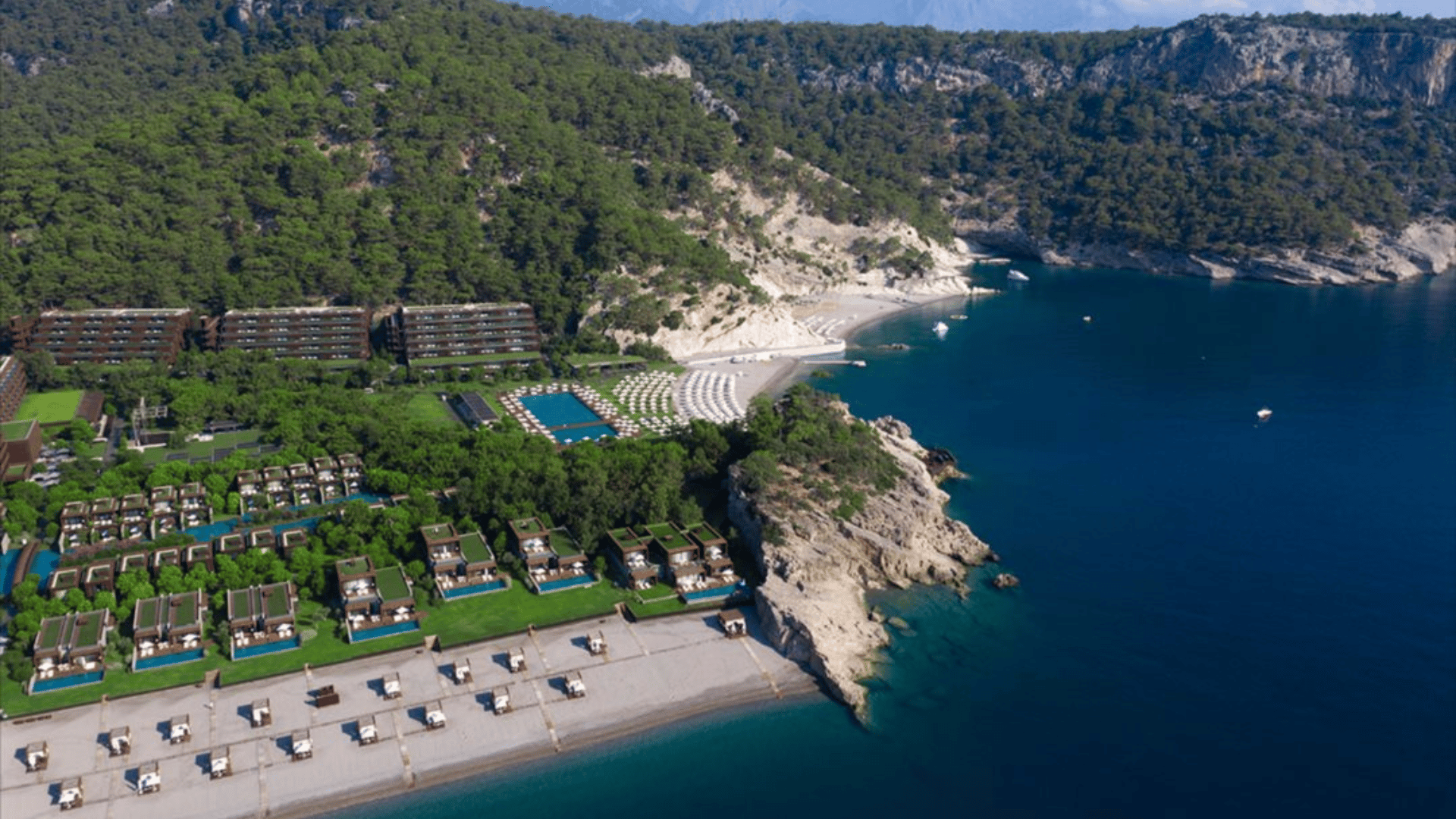 Luftaufnahme des Maxx Royal Kemer Resort zwischen bewaldeten Hängen und einer Bucht