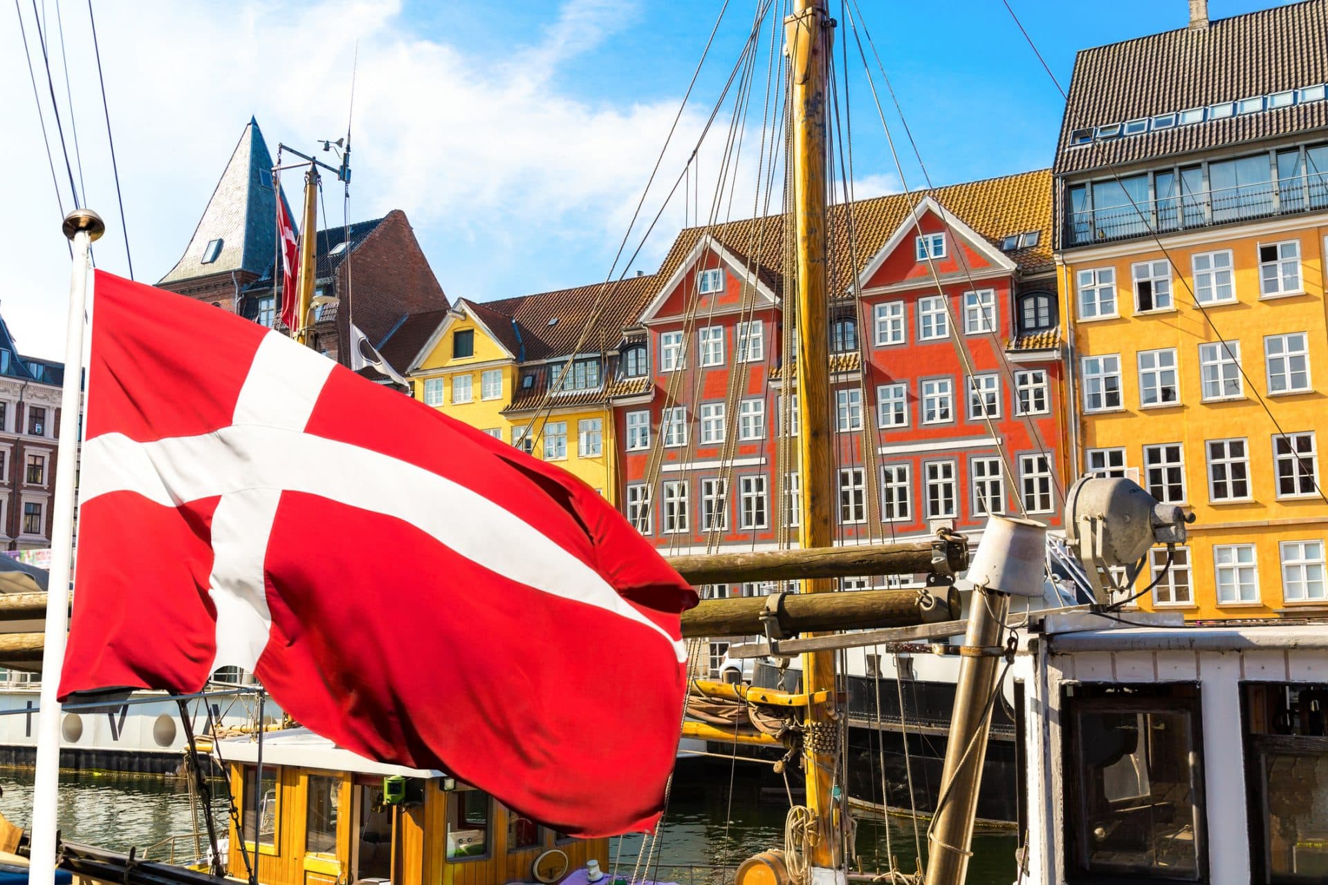 Copenhagen Iconic View. Famous Old Nyhavn Port In The Center Of Copenhagen, Denmark During Summer Sunny Day With Denmark Flag On The Foreground.