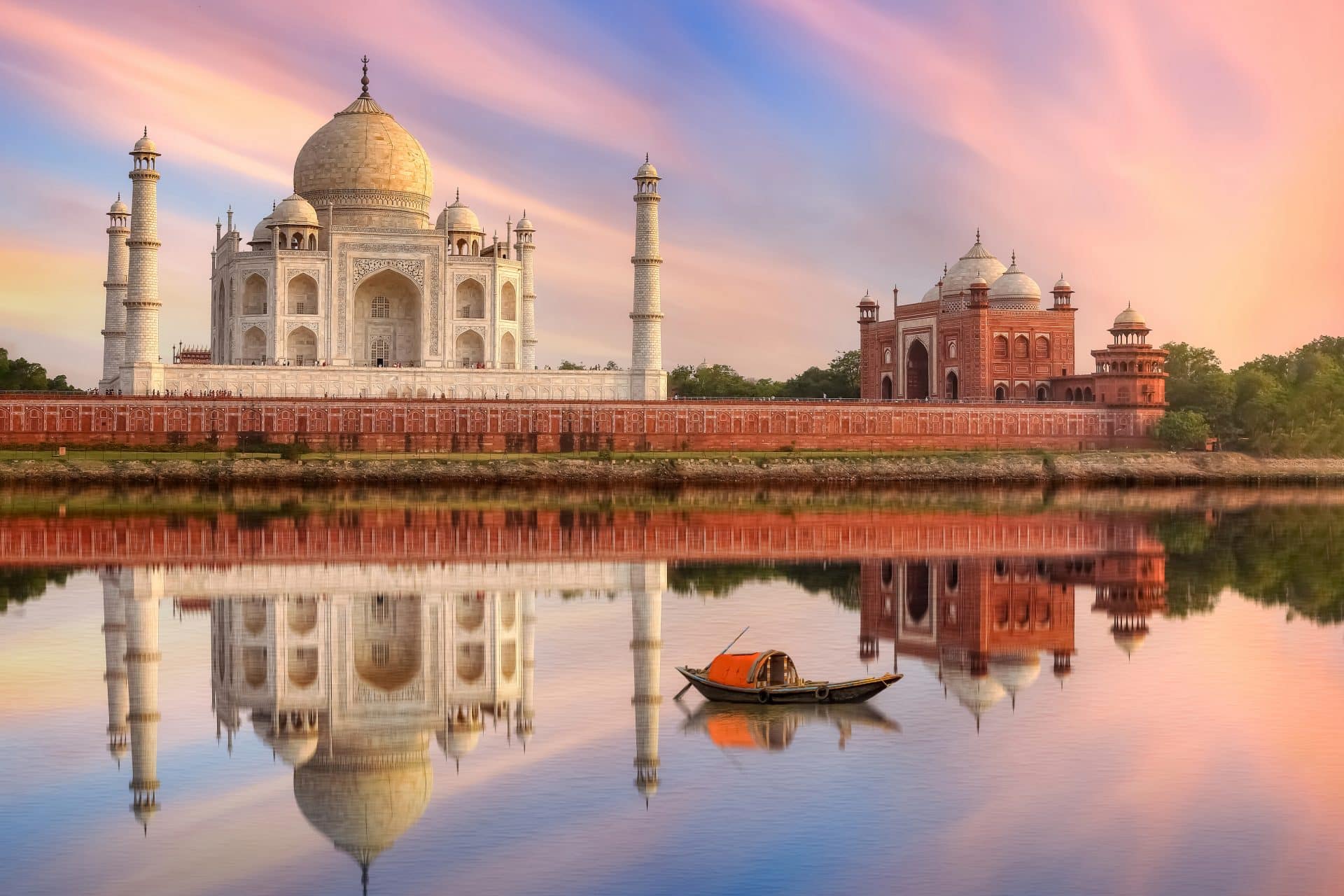 Taj Mahal Agra India At Sunset On The Banks Of River Yamuna With Moody Sunset Sky And View Of Wooden Boat Used For Tourist Ride On The River