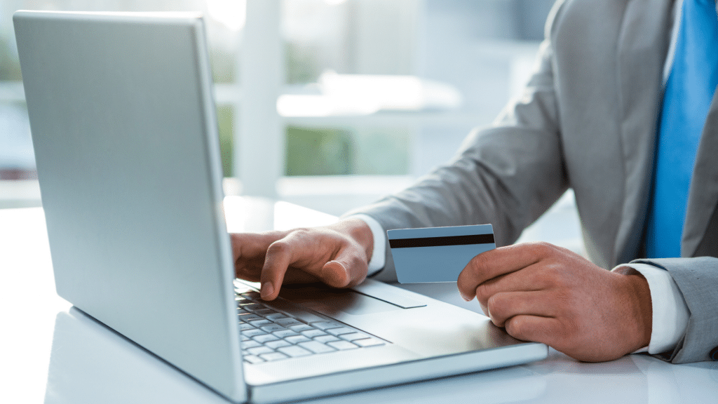 Mann im Anzug haelt Bankkarte in der Hand und tippt am Laptop