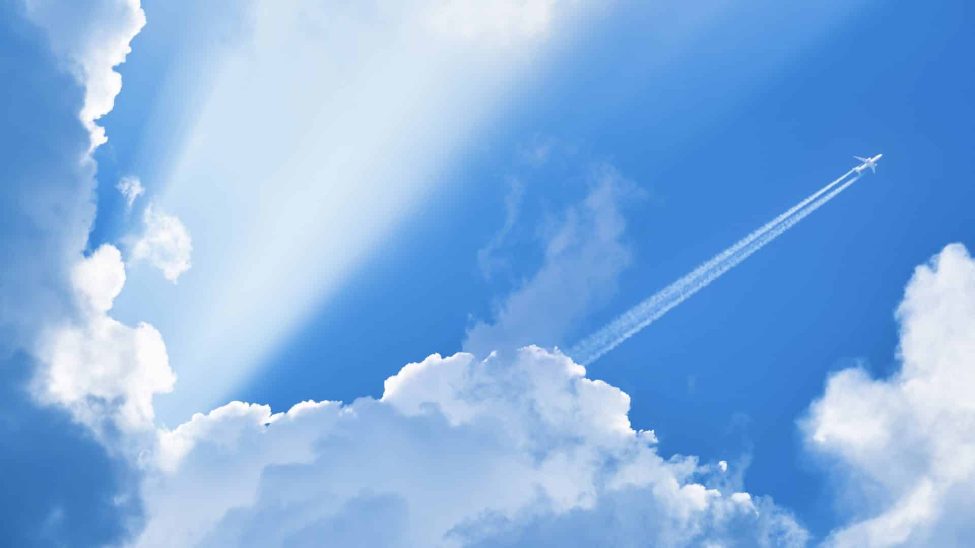 Airplane Flying In The Blue Sky Among Clouds And Sunlight