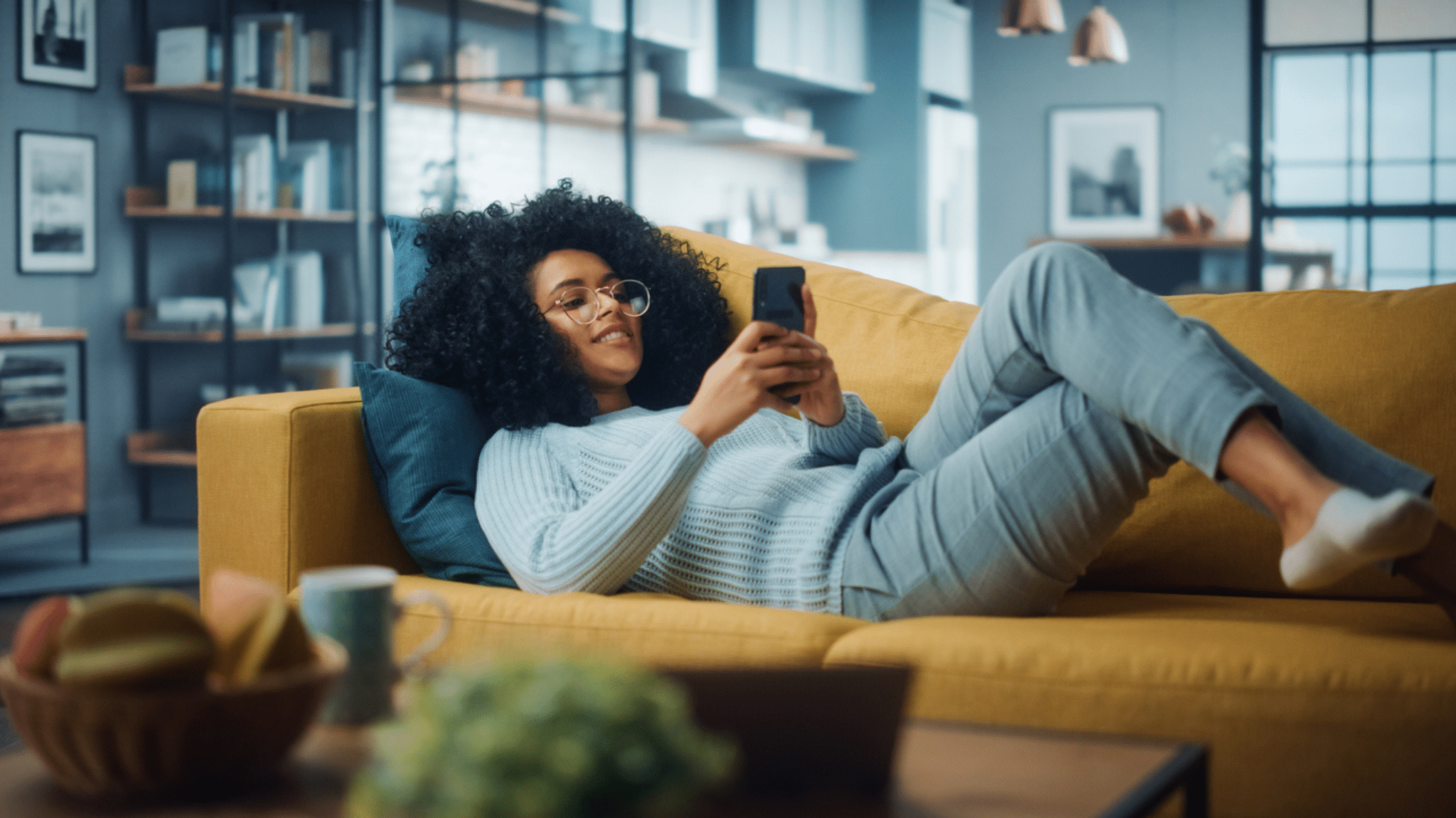 Frau liegt auf dem Sofa und tippt auf ihrem Smartphone