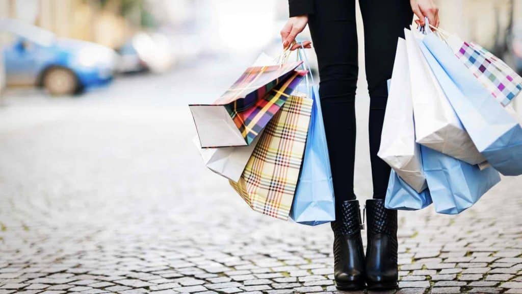 Frau steht auf einer Strasse und haelt mehrere Shoppingtueten in der Hand