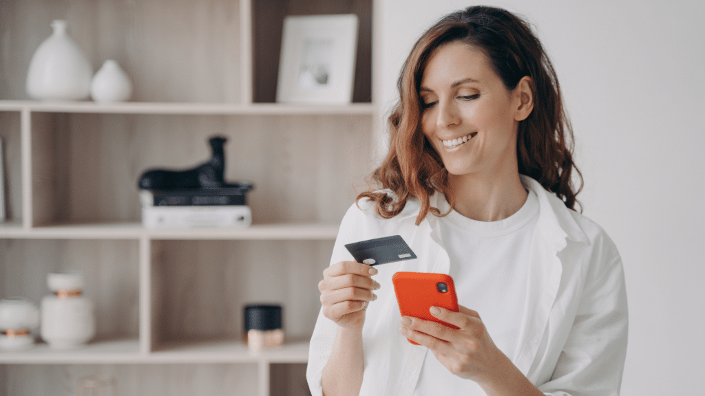 Laechelnde Frau haelt Handy und Bankkarte in der Hand