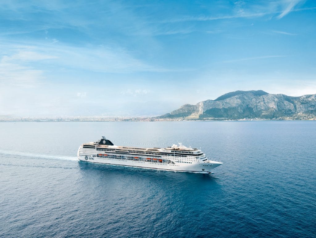 Die MSC Lirica faehrt vor einer Kueste mit Bergen auf offener See