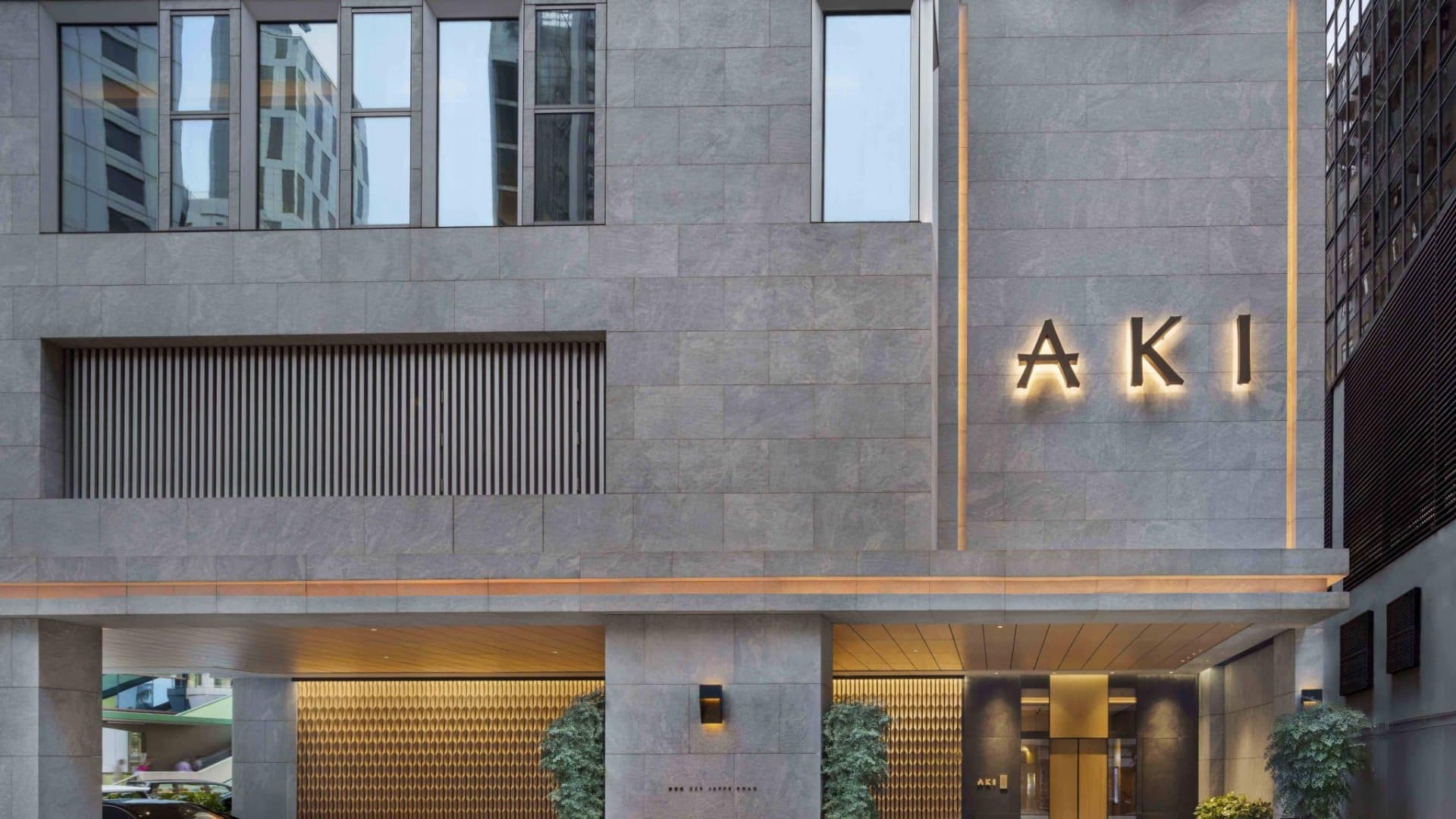 Steinfassade des AKI Hong Kong mit beleuchtetem Eingang in Wan Chai